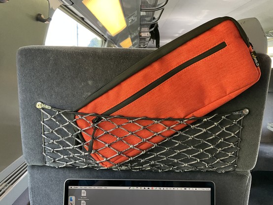 An orange keyboard bag in the net seat pocket on a TGV train.