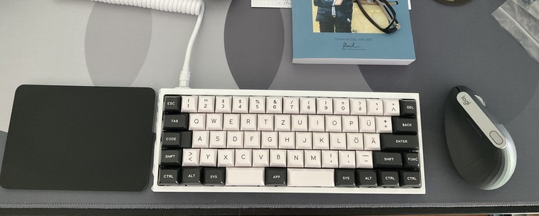 Photo of a desktop with (from left to right) a trackpad, a 60% keyboard, and a Logitech Vertical Mouse.