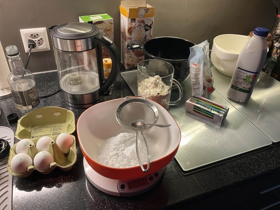 Küchenzeile mit aufgebauten Backzutaten: Eier, Butter, Milch, Puderzucker. Dazu noch Wasserkocher, Schüsseln, Waage