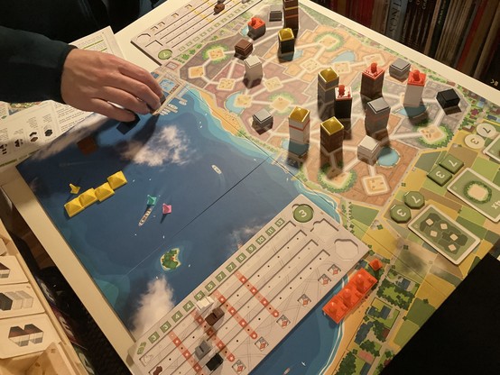 aufgeklapptes Spielfeld, eine Hand beim Bauen, einige Häuser stehen schon 