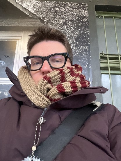 Frau in dicken beige-weinroten Schal gemummelt, weinrote Jacke an