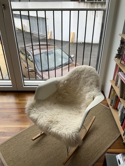 Photo of a rocking chair in front of a window, directly outside is a parked car.