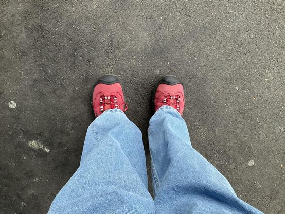 zwei helle Jeanshosenbeine und rote Keenschuhe drunter auf Asphalt 